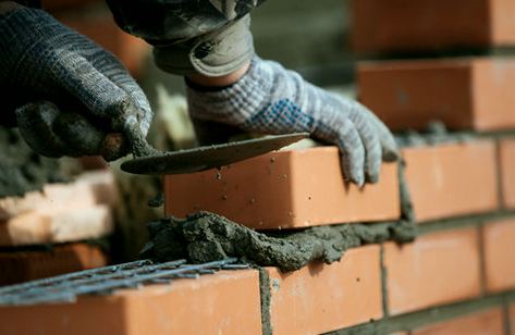Hands bedding brick courses into fresh mortar